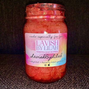 May include: A glass jar filled with a red whipped body butter. The jar has a label that reads "Lavish By Lilah" and "Whipped Body Butters".