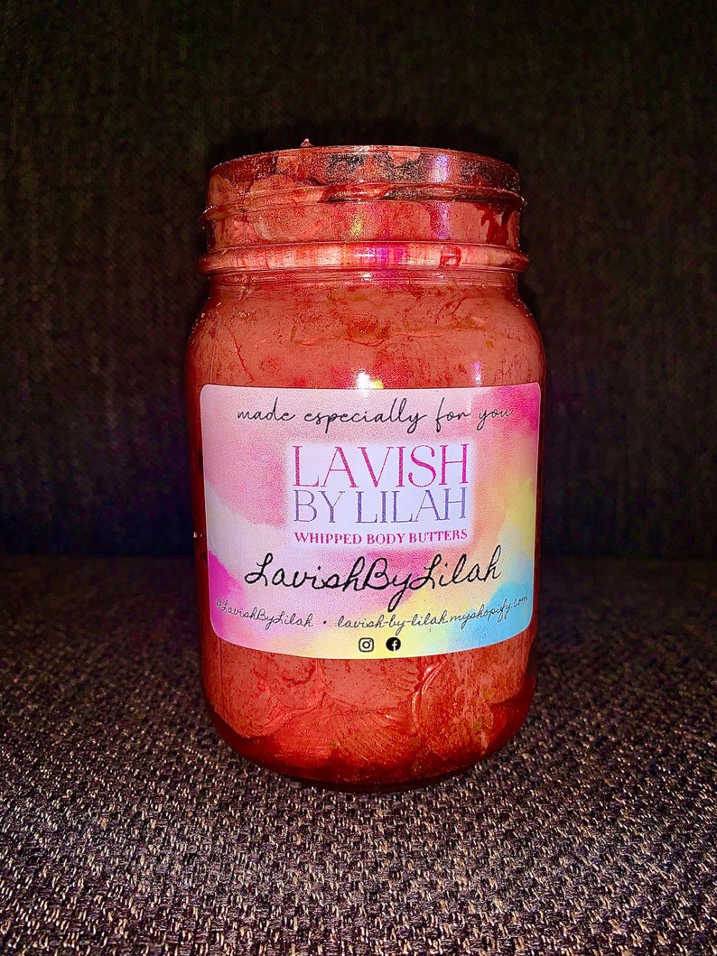 May include: A glass jar filled with a red whipped body butter. The jar has a label that reads "Lavish By Lilah" and "Whipped Body Butters".