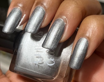 Może przedstawiać: Srebrny lakier do paznokci w butelce z metalicznym wykończeniem w kolorze srebrnym. Butelka jest oznaczona etykietą "Coco & Nails". Widoczna jest dłoń z paznokciami pomalowanymi srebrnym lakierem o metalicznym wykończeniu.
