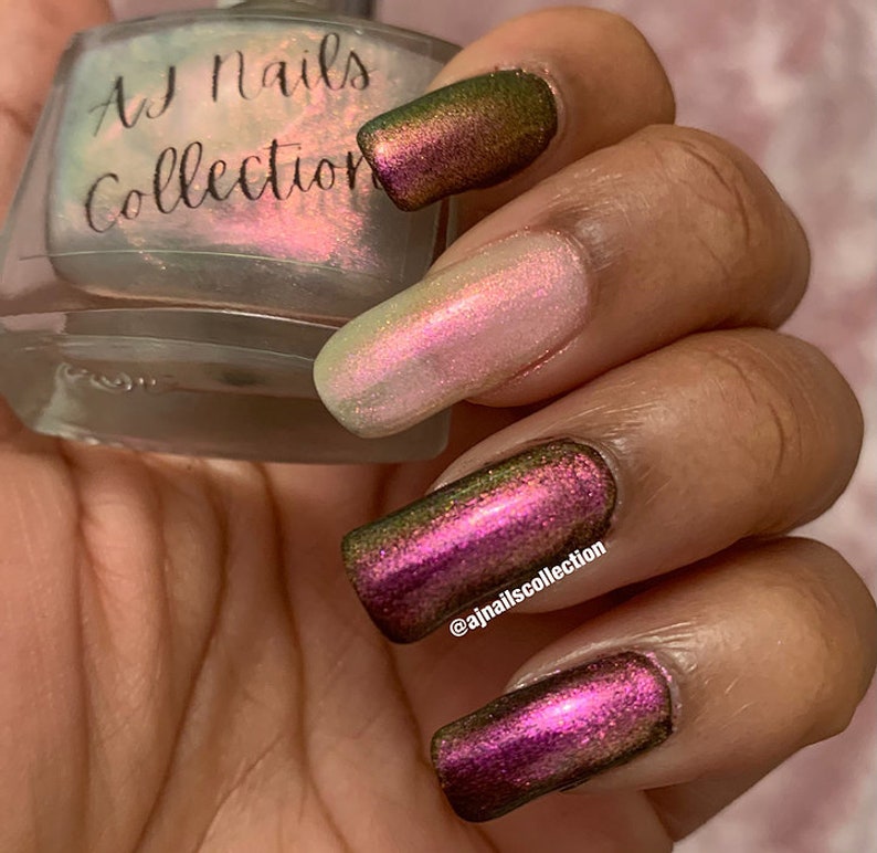 Puede incluir: Una mano de maniqu&iacute; con esmalte de u&ntilde;as iridiscente rosa claro, verde y morado. El esmalte de u&ntilde;as es de la colecci&oacute;n AJ Nails. El nombre de usuario de Instagram @ajnailscollection est&aacute; escrito en una de las u&ntilde;as.