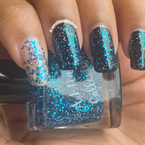 May include: Close-up of a hand with manicured nails. The nails are painted with a dark blue glitter polish, with some nails featuring a clear base with blue glitter. A bottle of nail polish is visible, with the text "ajnails collection".