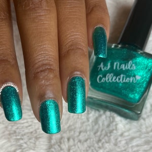 May include: A teal green nail polish bottle with a clear glass bottle and a black cap. The bottle has a label that says "AJ Nails Collection" with a heart symbol. The image shows a hand with four fingernails painted with the teal green nail polish.