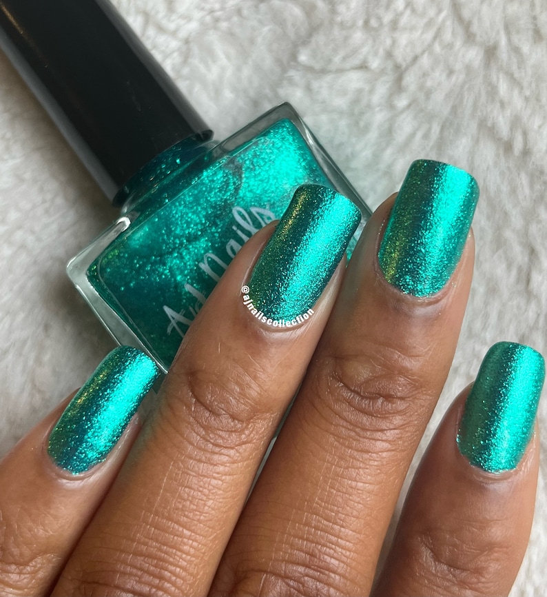 May include: A teal green nail polish with a shimmery finish. The polish is in a clear glass bottle with a black cap. The bottle is labelled "All Nails".