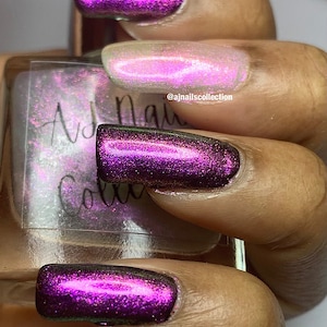 Puede incluir: Primer plano de una mano con cuatro u&ntilde;as pintadas con un esmalte de u&ntilde;as iridiscente de color morado oscuro. El esmalte de u&ntilde;as tiene un acabado brillante y refleja diferentes colores a la luz. La mano sostiene una peque&ntilde;a botella de esmalte de u&ntilde;as con el texto "AJ Nails Collection" en la etiqueta.