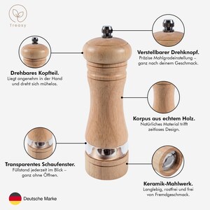 K&ouml;nnte beinhalten: Eine Pfefferm&uuml;hle aus Holz mit einem Edelstahlband und einem schwarzen Knopf. Die M&uuml;hle hat ein transparentes Fenster und Text, der "Drehbares Kopfteil" und "Deutsche Marke" lautet.