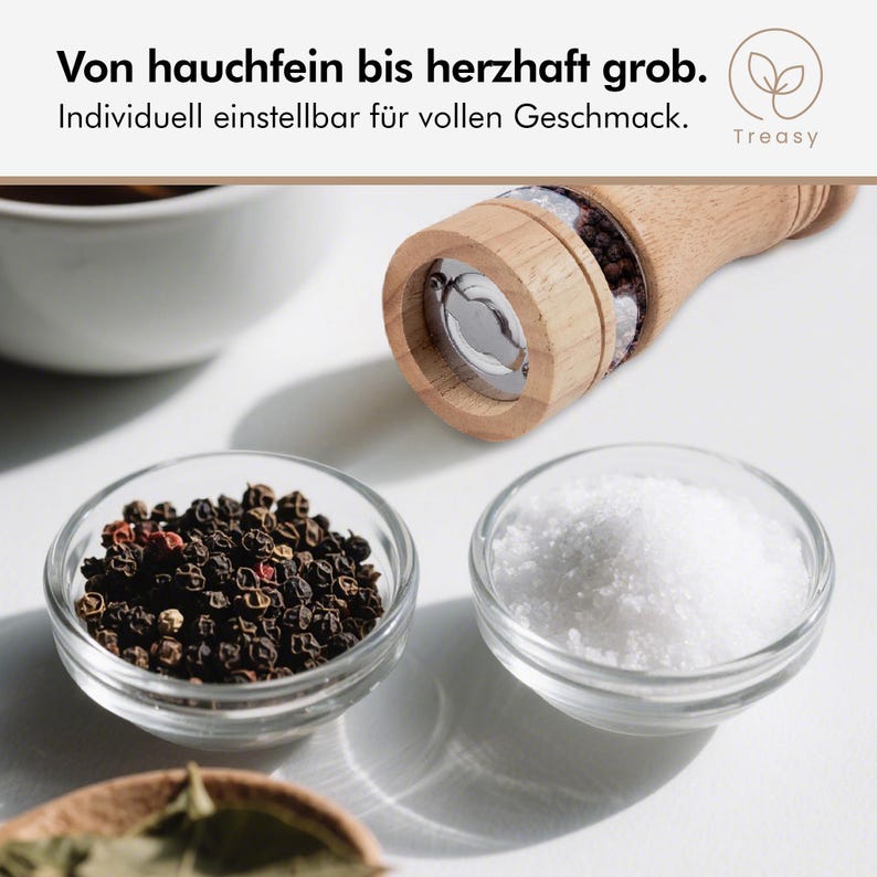 K&ouml;nnte beinhalten: Eine Pfefferm&uuml;hle aus Holz mit einem transparenten Glasteil, neben kleinen Glasschalen mit schwarzen Pfefferk&ouml;rnern und wei&szlig;em Salz. Der Text lautet: "Von hauchfein bis herzhaft grob. Individuell einstellbar f&uuml;r vollen Geschmack."