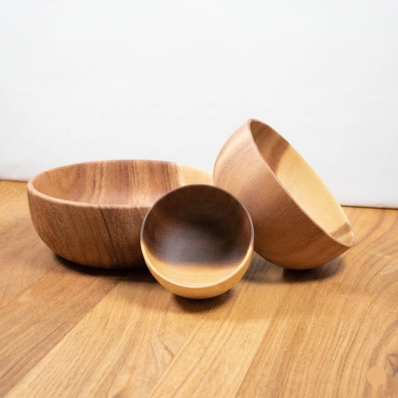 May include: Three wooden bowls of varying sizes. The largest bowl is wide and shallow, the smallest is a small, round bowl, and the third is a medium-sized bowl with a slanted rim. The bowls are made of light brown wood.