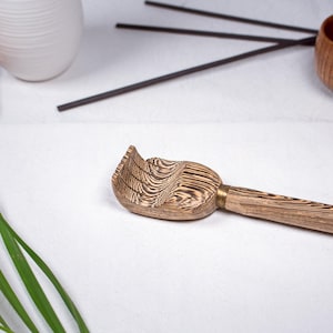 以下が含まれることがあります： 木製の孫の手。 湾曲したテクスチャード加工のヘッドと長いハンドルが付いています。 ヘッドは明るい茶色で、濃い茶色の木目模様があります。 真鍮色の金属片がヘッドをハンドルに接続しています。 ハンドルも明るい茶色です。