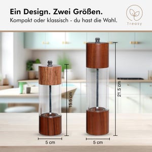 May include: Two wooden and glass pepper grinders, one 6.1 inches tall and the other 8.5 inches tall, each 2 inches wide. The grinders have a clear glass body and a wooden top and bottom. The text reads "Ein Design. Zwei Gr&ouml;&szlig;en. Kompakt oder klassisch - du hast die Wahl."