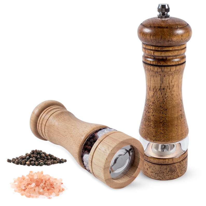 K&ouml;nnte beinhalten: Zwei Pfefferm&uuml;hlen aus Holz, eine aufrecht und eine auf der Seite, mit einem transparenten Abschnitt zur Ansicht des Inhalts. Schwarze Pfefferk&ouml;rner und rosa Himalaya-Salz werden neben den M&uuml;hlen gezeigt. Die M&uuml;hlen haben einen Edelstahl-Mahlmechanismus.