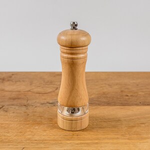 K&ouml;nnte beinhalten: Eine Pfefferm&uuml;hle aus Holz mit einem transparenten Acrylboden und einer Edelstahlplatte. Die M&uuml;hle besteht aus hellfarbigem Holz und steht auf einer Holzoberfl&auml;che. Das Design ist schlicht und klassisch.