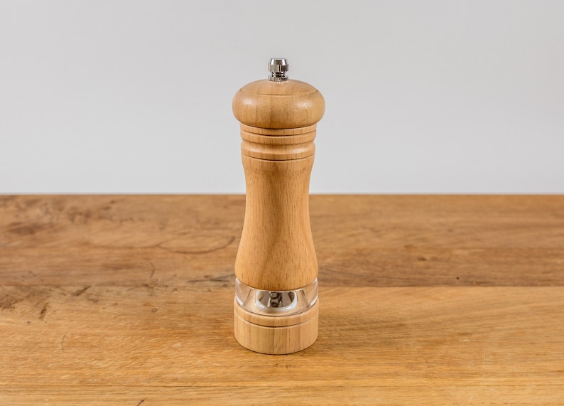 K&ouml;nnte beinhalten: Eine Pfefferm&uuml;hle aus Holz mit einem transparenten Acrylboden und einer Edelstahlplatte. Die M&uuml;hle besteht aus hellfarbigem Holz und steht auf einer Holzoberfl&auml;che. Das Design ist schlicht und klassisch.