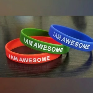 Könnte beinhalten: Drei Silikon-Armbänder in Rot, Grün und Blau mit dem Text "I AM AWESOME" in Weiß.