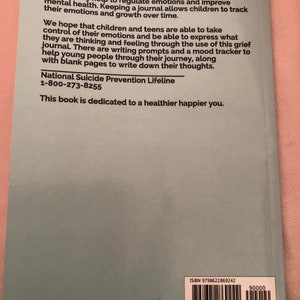 May include: A light blue book cover with white text. The text reads "Traumatic life events such as the death of a loved one, incarceration, divorce, sickness, or loss of a home can cause children and teens emotional and mental stress. Writing may help to regulate emotions and improve mental health. Keeping a journal allows children to track their emotions and growth over time. We hope that children and teens are able to take control of their emotions and be able to express what they are thinking and feeling through the use of this grief journal. There are writing prompts and a mood tracker to help young people through their journey, along with blank pages to write down their thoughts. National Suicide Prevention Lifeline 1-800-273-8255 This book is dedicated to a healthier happier you."