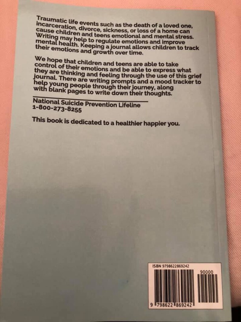 May include: A light blue book cover with white text. The text reads "Traumatic life events such as the death of a loved one, incarceration, divorce, sickness, or loss of a home can cause children and teens emotional and mental stress. Writing may help to regulate emotions and improve mental health. Keeping a journal allows children to track their emotions and growth over time. We hope that children and teens are able to take control of their emotions and be able to express what they are thinking and feeling through the use of this grief journal. There are writing prompts and a mood tracker to help young people through their journey, along with blank pages to write down their thoughts. National Suicide Prevention Lifeline 1-800-273-8255 This book is dedicated to a healthier happier you."