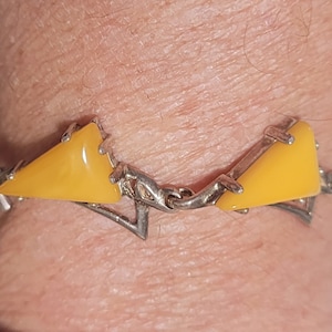 May include: A silver bracelet featuring yellow triangular stones. The bracelet is crafted from a delicate chain with intricate details.