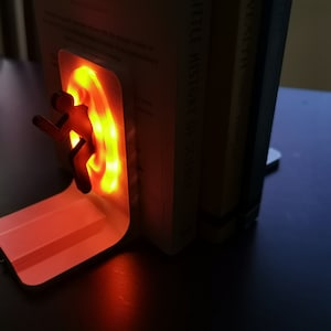 May include: A white bookend with a glowing orange portal and a black silhouette of a person running through it. The bookend is on a dark surface.