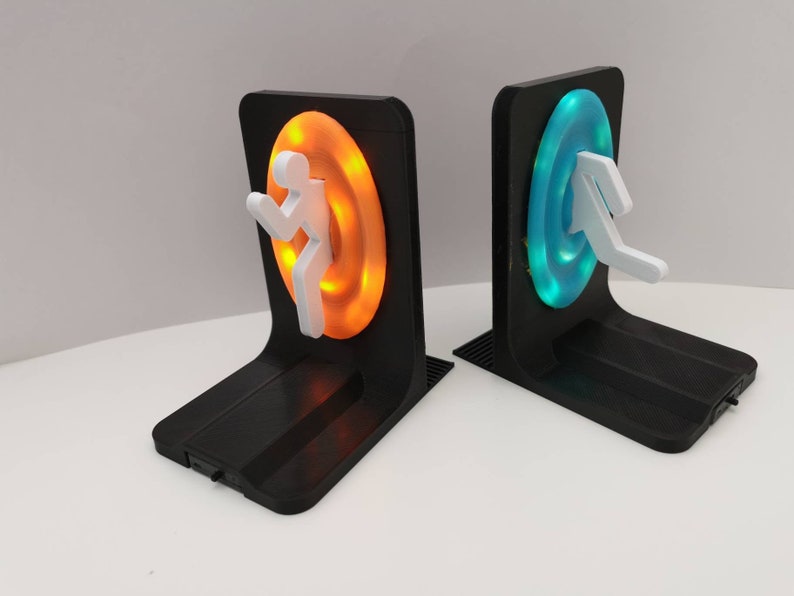 May include: A pair of black bookends with a glowing orange and blue portal design. Each portal has a white figure running through it.