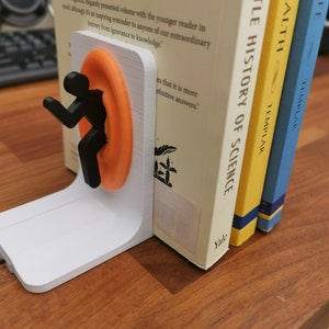 May include: A white 3D printed bookend featuring a black silhouette of a person entering a bright orange portal. The bookend is holding up two books, one titled "A Little History of Science" by Bill Bryson and the other titled "Health" by Templar.