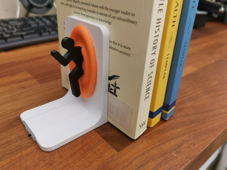 May include: A white 3D printed bookend featuring a black silhouette of a person entering a bright orange portal. The bookend is holding up two books, one titled "A Little History of Science" by Bill Bryson and the other titled "Health" by Templar.