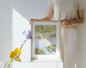 Könnte beinhalten: Ein gerahmtes Aquarellbild, das einen Teich mit grünen Seerosenblättern und kleinen rosa Blüten in sanften Blau- und Grüntönen zeigt. Der Text The Wallflowers Effect ist in der unteren rechten Ecke des Rahmens aufgedruckt.