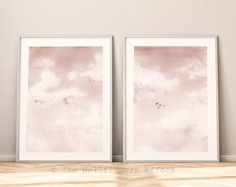 Puede incluir: Dos láminas de arte mural verticales enmarcadas que muestran un cielo en acuarela en tonos rosa empolvado y blanco con nubes suaves. La lámina derecha incluye una pequeña silueta de aves en vuelo. El texto The Wallflowers Effect es visible.