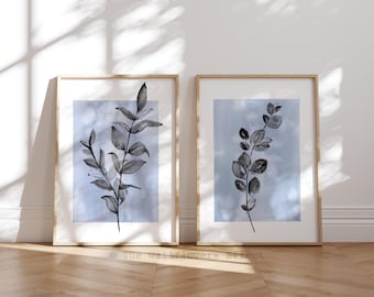 Può includere: Due stampe da parete incorniciate con illustrazioni botaniche a inchiostro nero di rami frondosi centrati su uno sfondo acquerello blu tenue. Ogni stampa è racchiusa in una cornice di legno chiaro con il testo The Wallflowers Effect.
