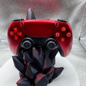 May include: A red and black gaming controller resting on a black, geometric stand. The controller has red buttons and directional pad. The stand has a jagged, crystal-like design, with red accents. The controller is a modern gaming accessory.