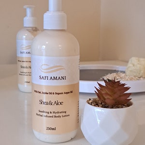 Może przedstawiać: Dwie białe butelki z pompką z balsamem do ciała i brązową etykietą. Etykieta zawiera napis "Safi Amani" i "Shea & Aloe" z tekstem "Soothing & Hydrating Herbal Infused Body Lotion" i "250ml".