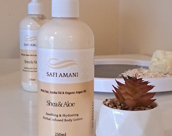 Może przedstawiać: Dwie białe butelki z pompką z balsamem do ciała i brązową etykietą. Etykieta zawiera napis "Safi Amani" i "Shea & Aloe" z tekstem "Soothing & Hydrating Herbal Infused Body Lotion" i "250ml".