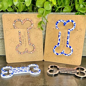 May include: Two wooden bone-shaped bookmarks with leopard print designs. One bookmark is pink and white, the other is blue and white. The bookmarks have the text "Books are dog gone good!" printed on them.