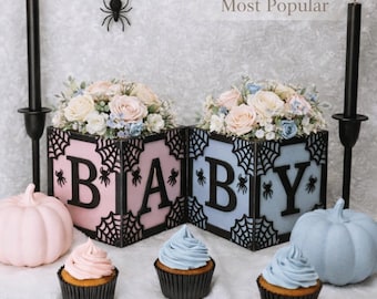 May include: Two square boxes labeled B, A, B, Y with black spiderweb cutouts, pink and blue panels, and floral arrangements. Includes text 6x6 Size Most Popular, black candles, pink and blue pumpkins, and frosted cupcakes.