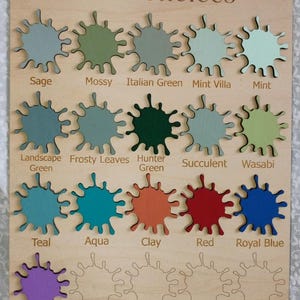 May include: A rectangular wooden board titled Paint Choices featuring fifteen painted wooden paint splatters in various colours including sage, mossy, Italian green, mint villa, mint, landscape green, frosty leaves, hunter green, succulent, wasabi, teal, aqua, clay, red, royal blue, and violet.