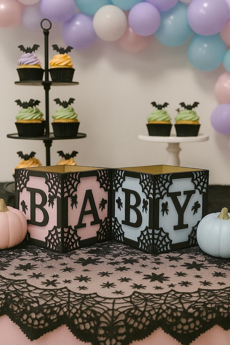 Pode incluir: Caixas rosa e azuis com a palavra "BABY" com um design de teia de aranha, perfeitas para um ch&aacute; de beb&eacute; com tema de Halloween. Cupcakes com coberturas de morcego e ab&oacute;boras decorativas completam a cena festiva.
