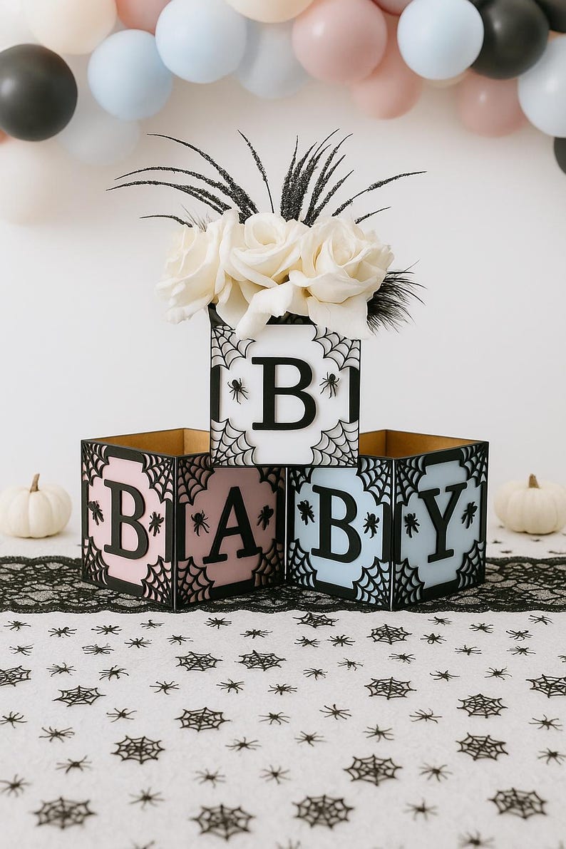 Pode incluir: Decora&ccedil;&atilde;o de ch&aacute; de beb&eacute; com tr&ecirc;s blocos que formam a palavra "BABY". Os blocos pretos apresentam desenhos de teias de aranha e as letras s&atilde;o rosa, brancas e azul claro. Rosas brancas e bal&otilde;es completam o ambiente festivo.