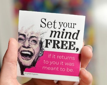 Op de afbeelding: Een witte kaart met roze tekst die luidt: "Maak je geest vrij, als het terugkomt, was het bedoeld om te zijn." De kaart toont een kleurrijke illustratie van een lachend persoon.