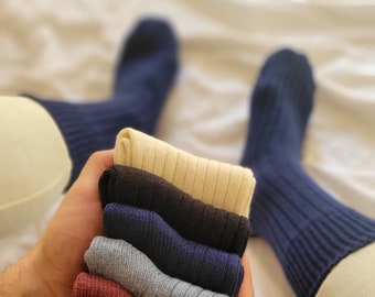 May include: A stack of eight pairs of socks in various colors, including gray, brown, blue, and beige. The socks are folded and arranged in a pile, with the top sock being beige.