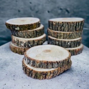 May include: A stack of wooden round slices, each with a natural bark edge, arranged in a pyramid shape. The top slice is larger than the others and is a natural wood color. The slices are perfect for crafting or home decor.