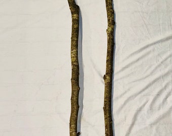 May include: Two long, brown, and gray branches with bark. The branches are straight and have a natural, rustic look.