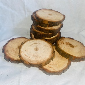 May include: A stack of eight natural wood round slices, with the top slice and the bottom slice laying flat on a white surface. The wood slices are approximately 4 inches in diameter.
