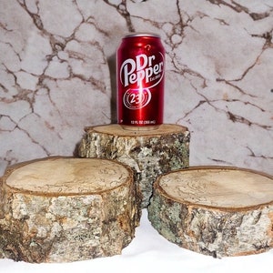 May include: Three round wooden slices, or coasters, made from tree bark, with a red can of Dr Pepper on top of the middle slice.