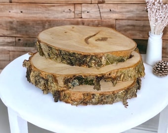 May include: Three wooden slices stacked on top of each other. The slices are round and have a natural bark edge. The wood is a light brown color.
