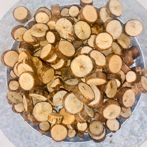 May include: A bowl filled with numerous round, wooden slices, all of a similar size and shape. The slices are a light brown color and have a natural, rustic appearance.