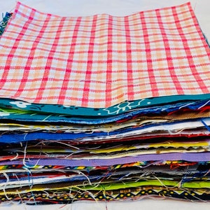 Puede incluir: Una pila de cuadrados de tela coloridos, que muestran una variedad de patrones y colores. La capa superior presenta un dise&ntilde;o a cuadros rojos y blancos. Otras telas incluyen textiles florales, lisos y estampados, ideales para proyectos de costura o manualidades.