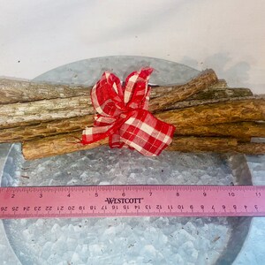 May include: A bundle of brown sticks tied together with a red and white checkered ribbon. The sticks are approximately 10 inches long and are arranged in a fan shape. The sticks are on a silver metal surface.