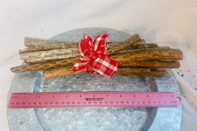 May include: A bundle of brown sticks tied together with a red and white checkered ribbon. The sticks are approximately 10 inches long and are arranged in a fan shape. The sticks are on a silver metal surface.