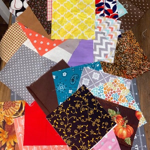 Puede incluir: Una colecci&oacute;n de cuadrados de tela en varios patrones y colores, incluyendo b&eacute;isbol, lunares, dise&ntilde;os florales y geom&eacute;tricos. Las telas est&aacute;n dispuestas sobre una esterilla de corte, mostrando una variedad de texturas e impresiones adecuadas para proyectos de acolchado o manualidades.