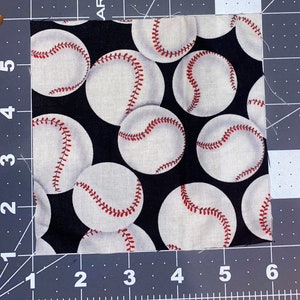 Puede incluir: Trozo de tela cuadrado con un patr&oacute;n repetido de pelotas de b&eacute;isbol blancas con costuras rojas sobre un fondo negro. La tela est&aacute; sobre una esterilla de corte gris con medidas en cent&iacute;metros. Las pelotas de b&eacute;isbol est&aacute;n espaciadas uniformemente.