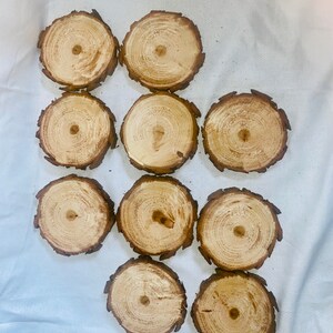 May include: Ten round wooden coasters with a natural wood finish. The coasters are made from tree slices and have a rustic look.