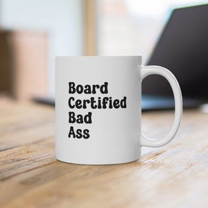 May include: White ceramic coffee mug with black text that reads "Board Certified Bad Ass".